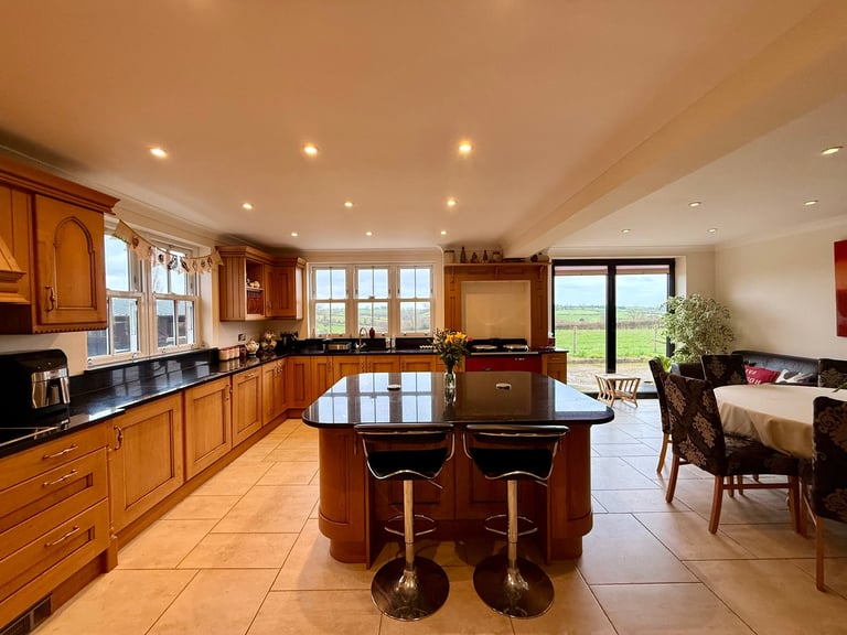 Modern open-plan kitchen with wooden cabinetry, island with seating, and living area visible in the background
