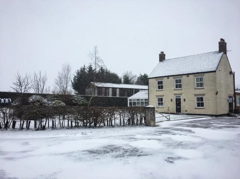 Yellow brick countryside farmhouse with outbuildings in snowy winter landscape with bare trees