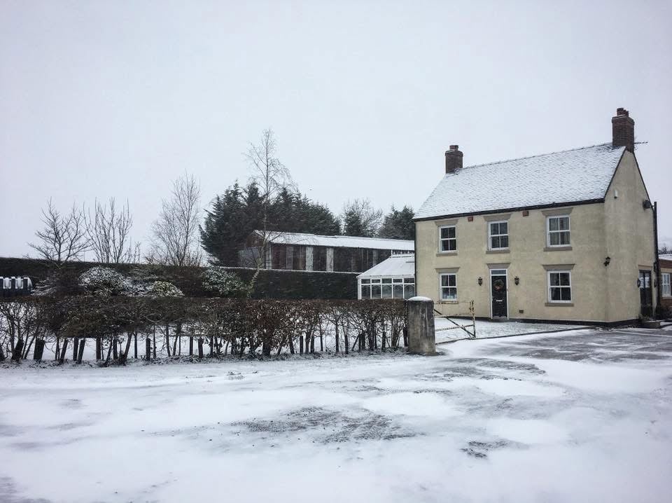 Yellow brick farmhouse with render exterior and outbuildings surrounded by snowy fields and bare trees in winter