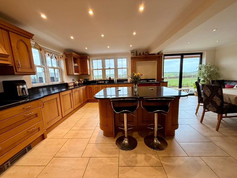 Spacious luxury kitchen with wooden cabinetry, large island with seating, multiple windows, recessed lighting, and countryside views