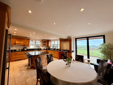Spacious open-concept kitchen and dining area with wood cabinetry, island, round table, and expansive windows overlooking green countryside