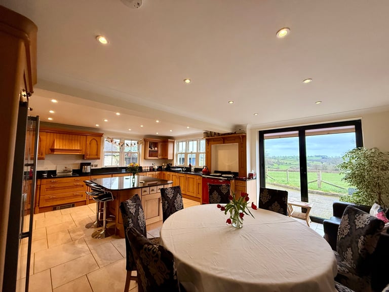 Spacious open-concept kitchen and dining area with wood cabinetry, island, round table, and expansive windows overlooking green countryside
